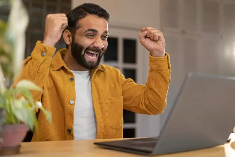 Imagem de uma pessoa comemorando com os braços erguidos em frente ao computador